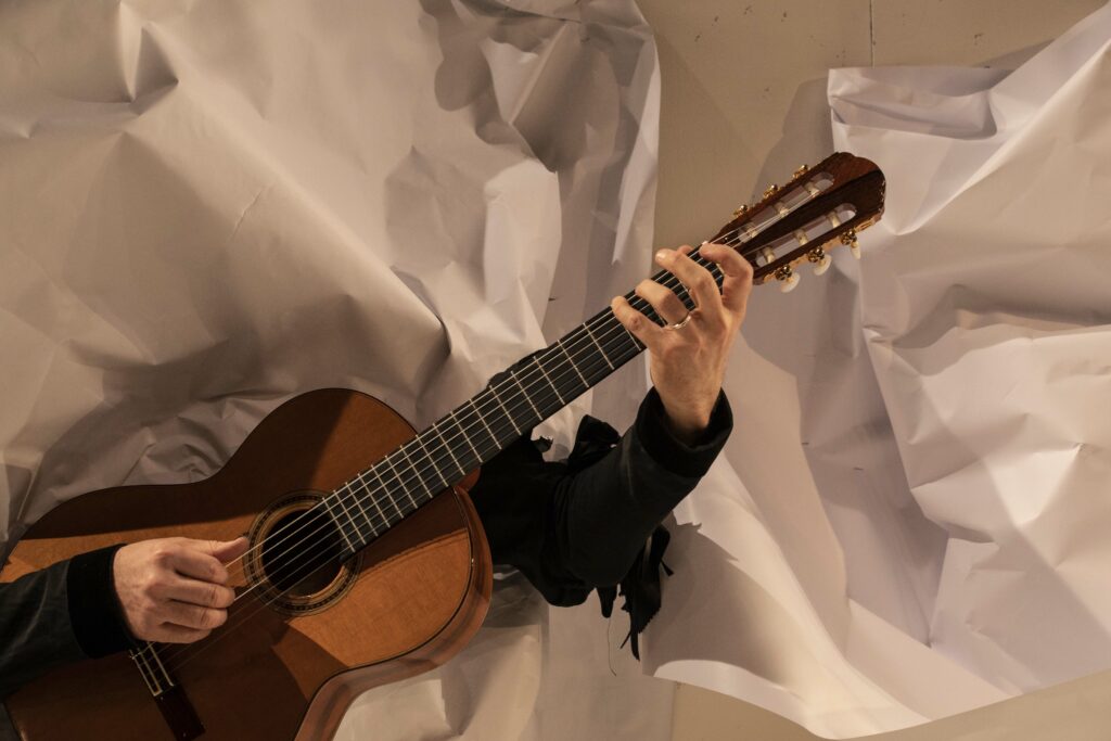 Guitare jouée par Richard Comte apparaissant à travers le papier déchiré du décors de Baùbo