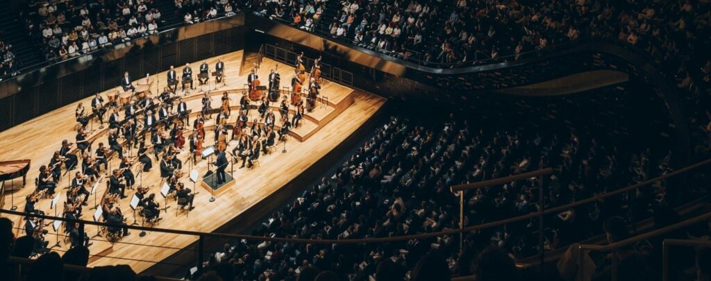 La photo est une prise de vue en hauteur lors d'un concert sur l'orchestre illuminé et les spectateurs à la philharmonie.